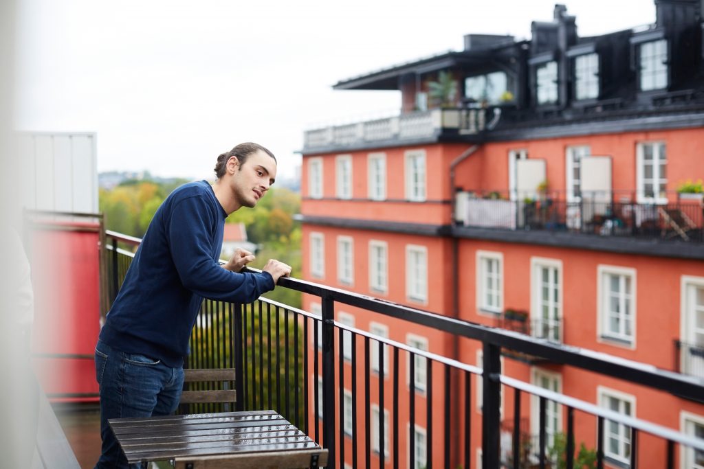 Ung mann står å ser ut fra balkong