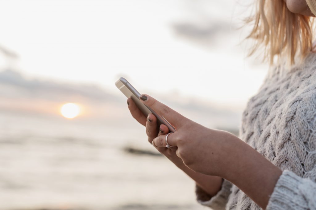 En dame med telefon i hånden og solnedgang