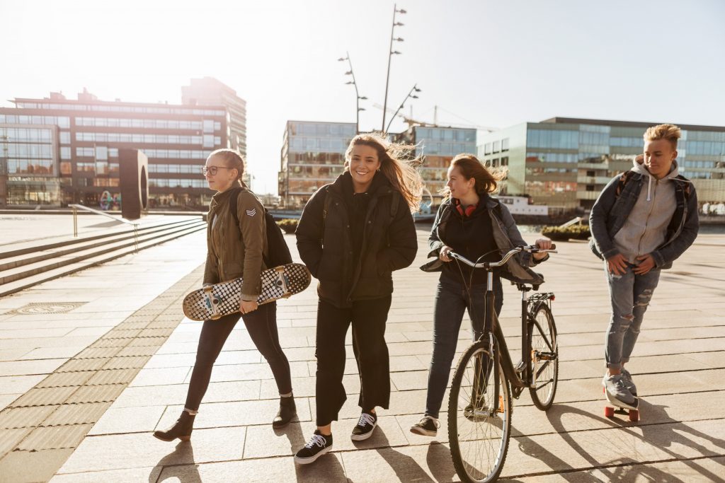 Unge venner går med skateboards og sykkel på torg