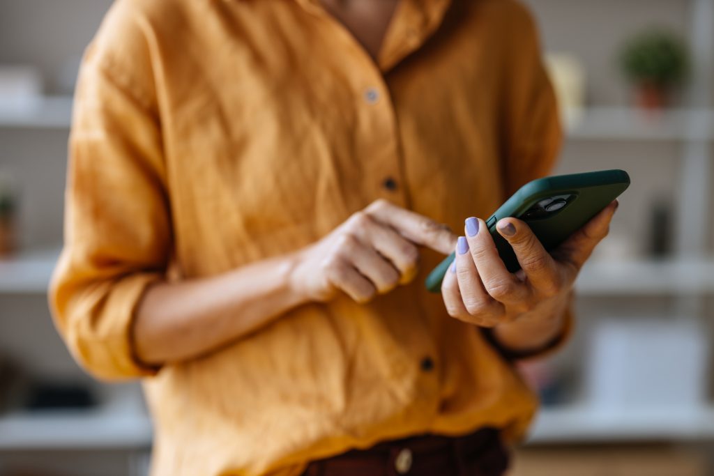 Dame med orange skjorte holder en mobiltelefon med grønt deksel.