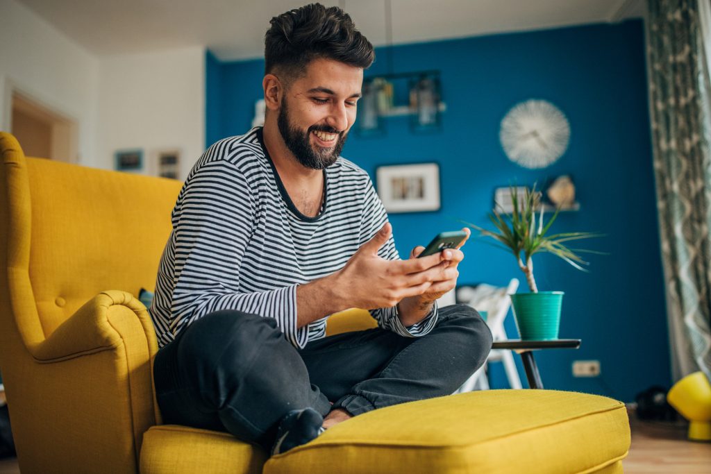 Blid mann som holder en telefon - Sitter i en gul stol
