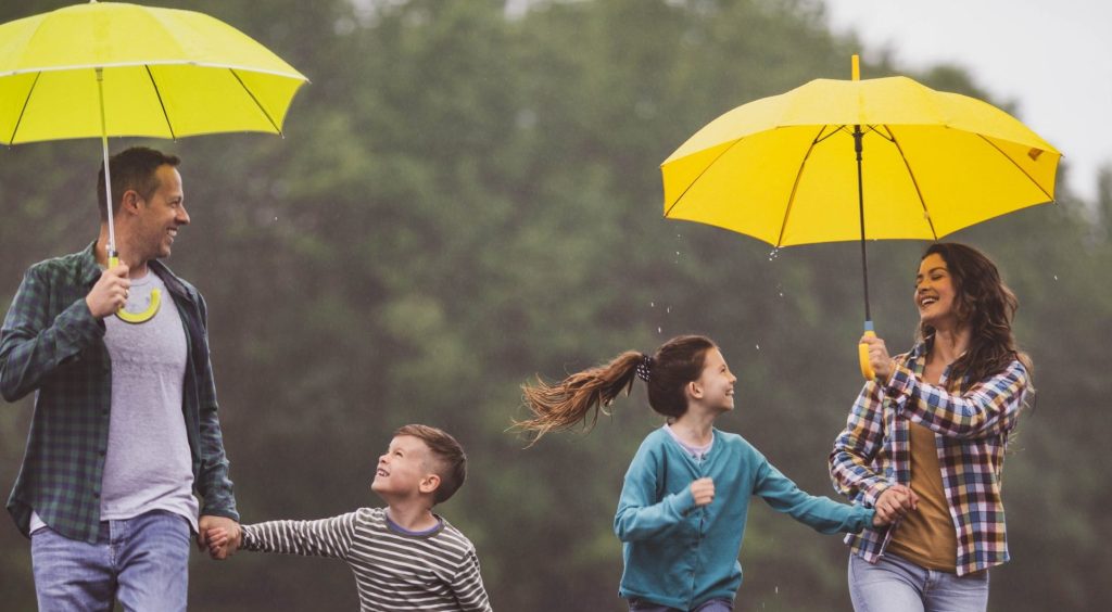 Høstbilde med familie i regn som smiler. De har gule paraplyer.