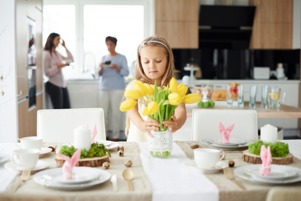 Liten jente dekker bordet til påske med gule liljer